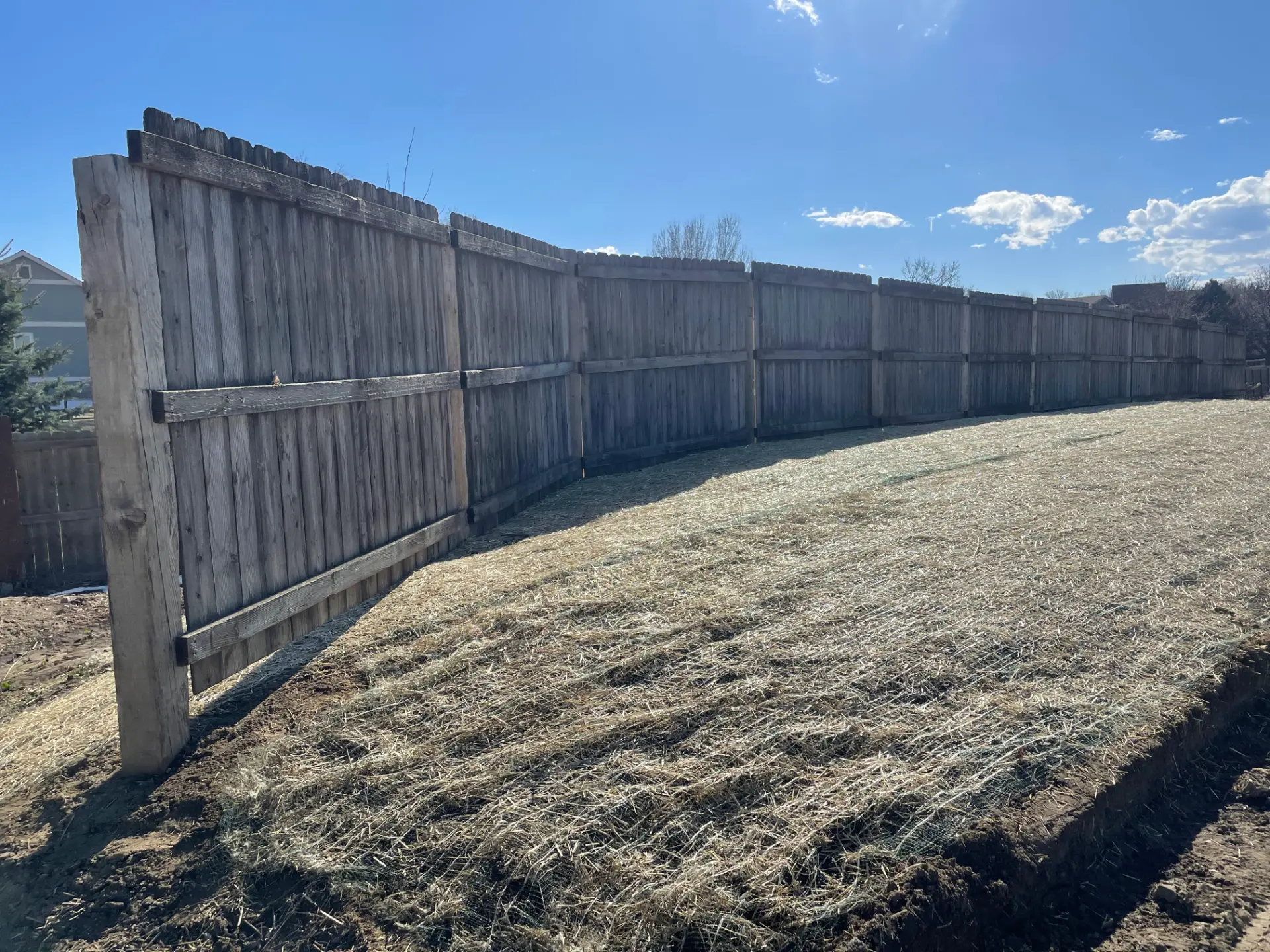 Long weathered wood privacy fence following a sloped residential property line