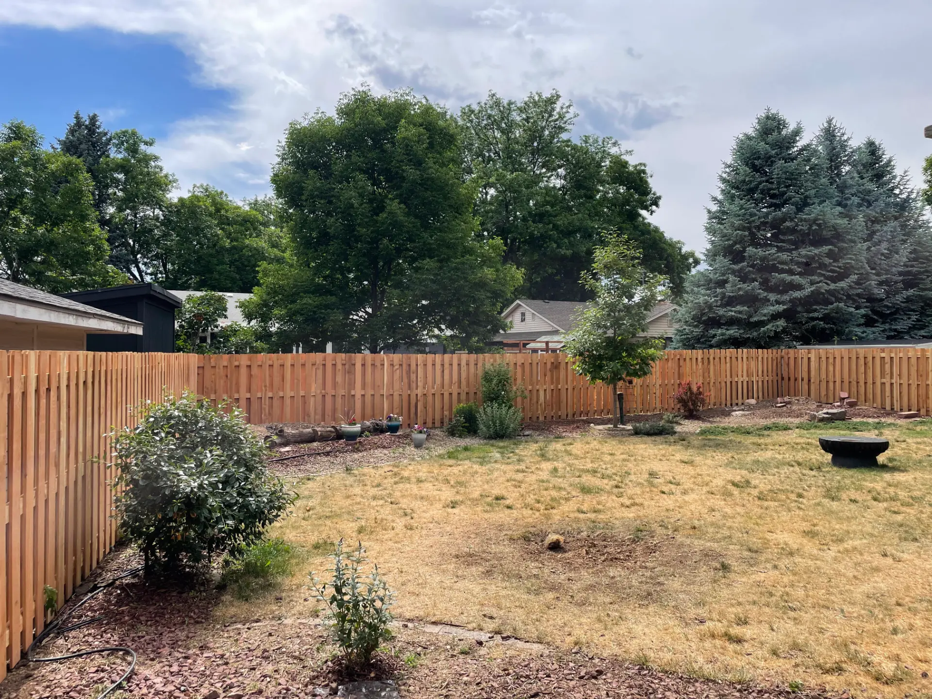 New cedar picket fence wrapping around a landscaped residential backyard
