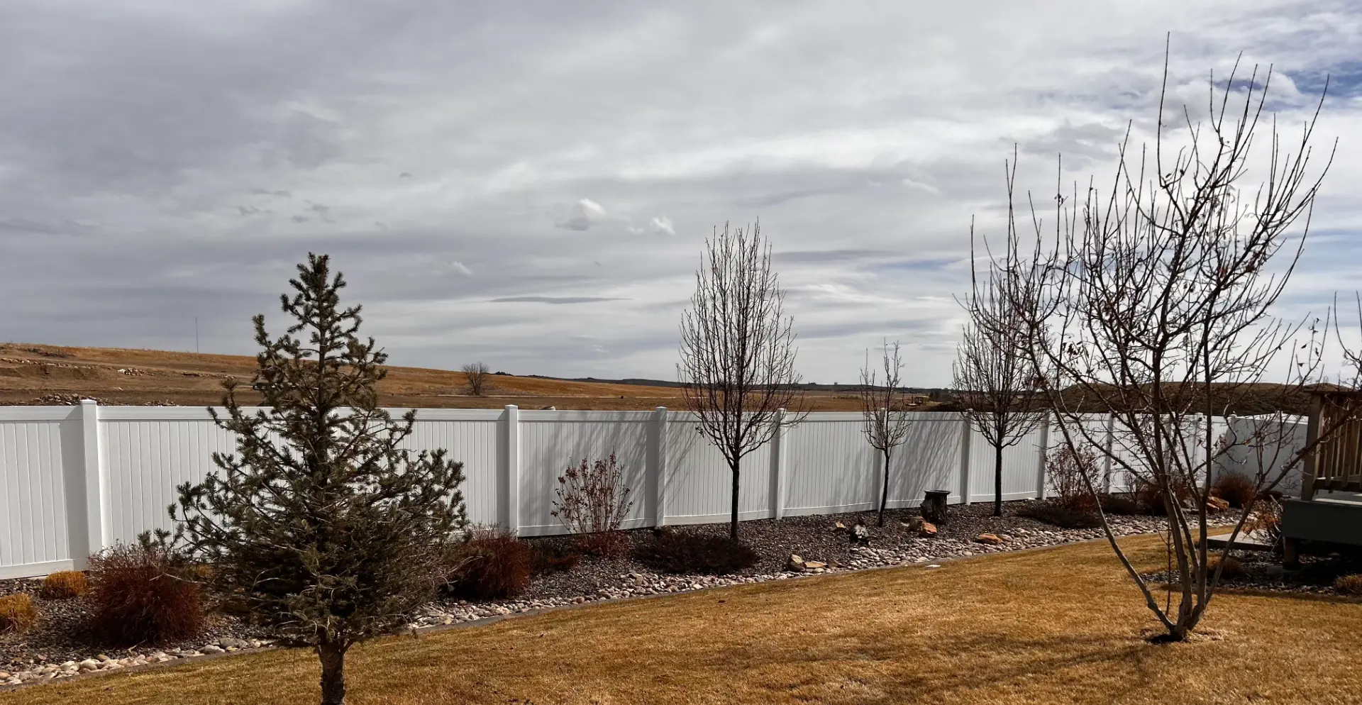 Long white vinyl privacy fence bordering a landscaped backyard with trees and shrubs