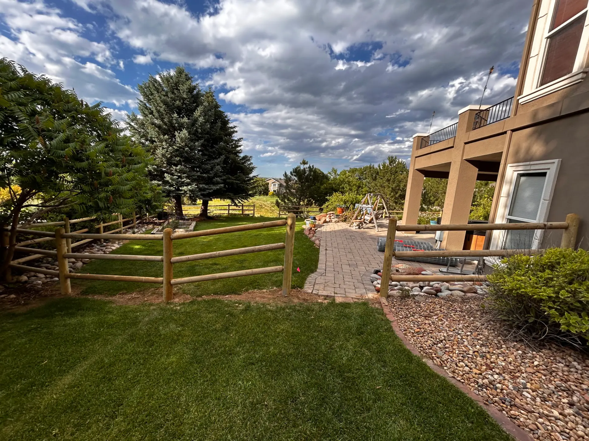 New round-post split rail fence surrounding a landscaped backyard