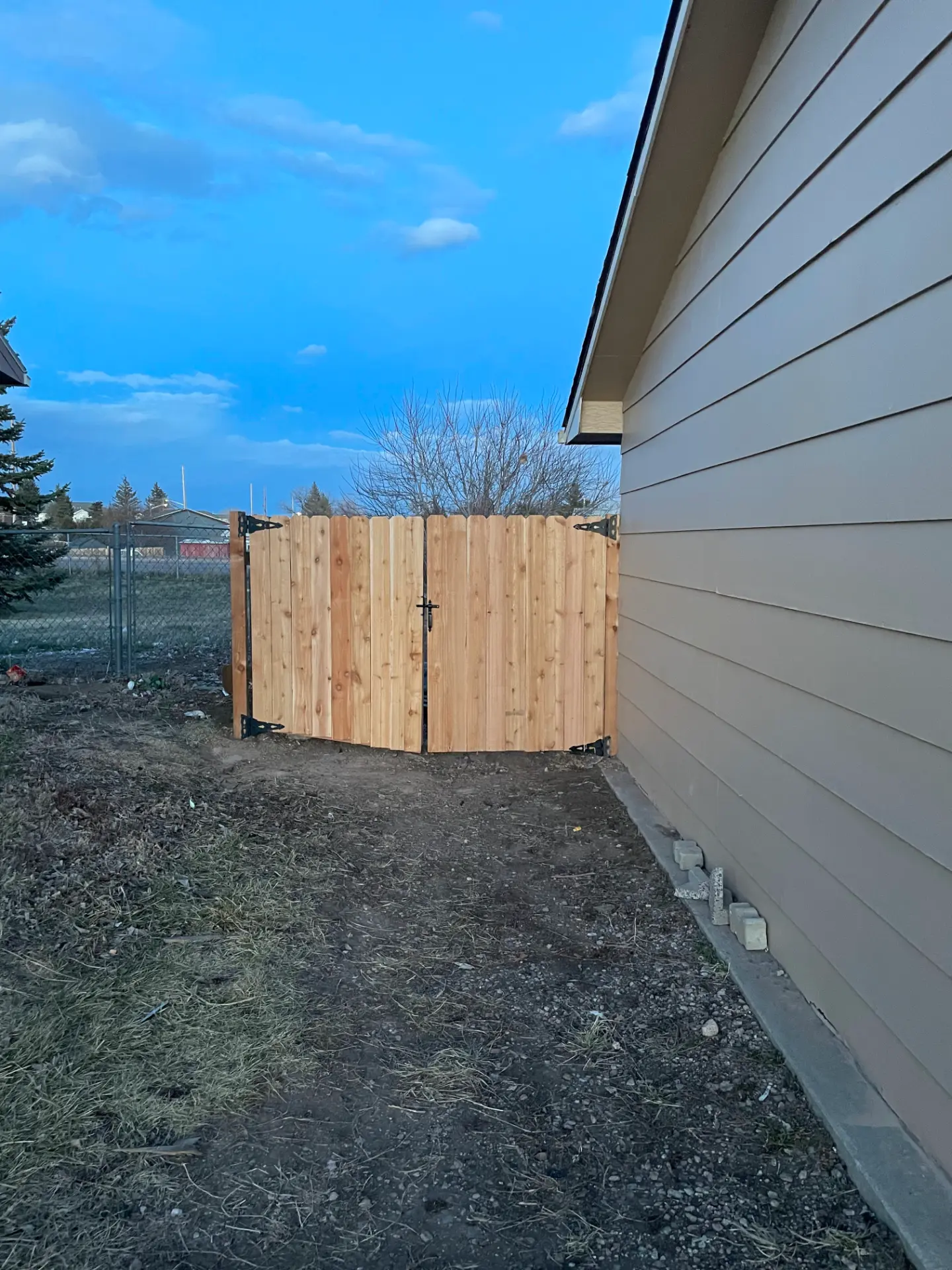 Natural cedar double walk gate with black hinges and latch beside a home