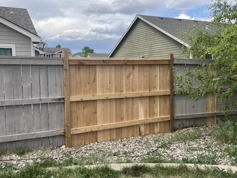 New cedar gate panel set between weathered wood fences along a rock border