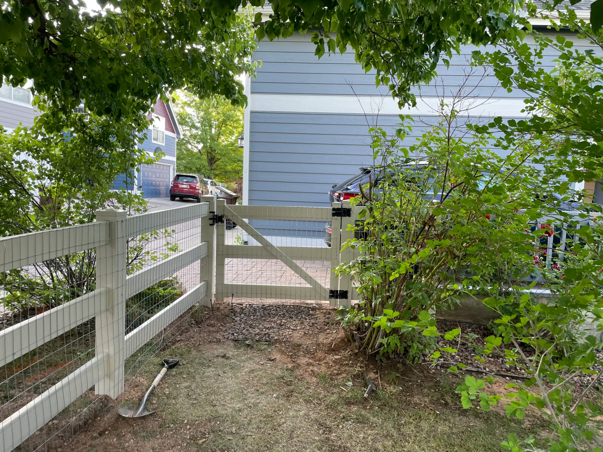 White three-rail walk gate with wire mesh and black hardware beside a home