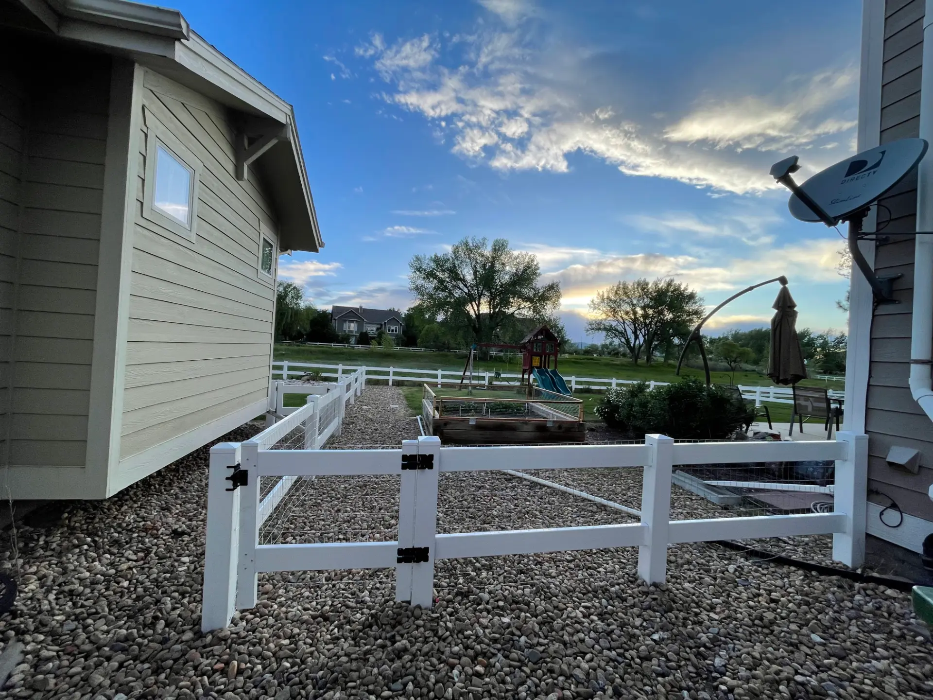 White ranch rail fence with wire mesh and a double gate between two homes