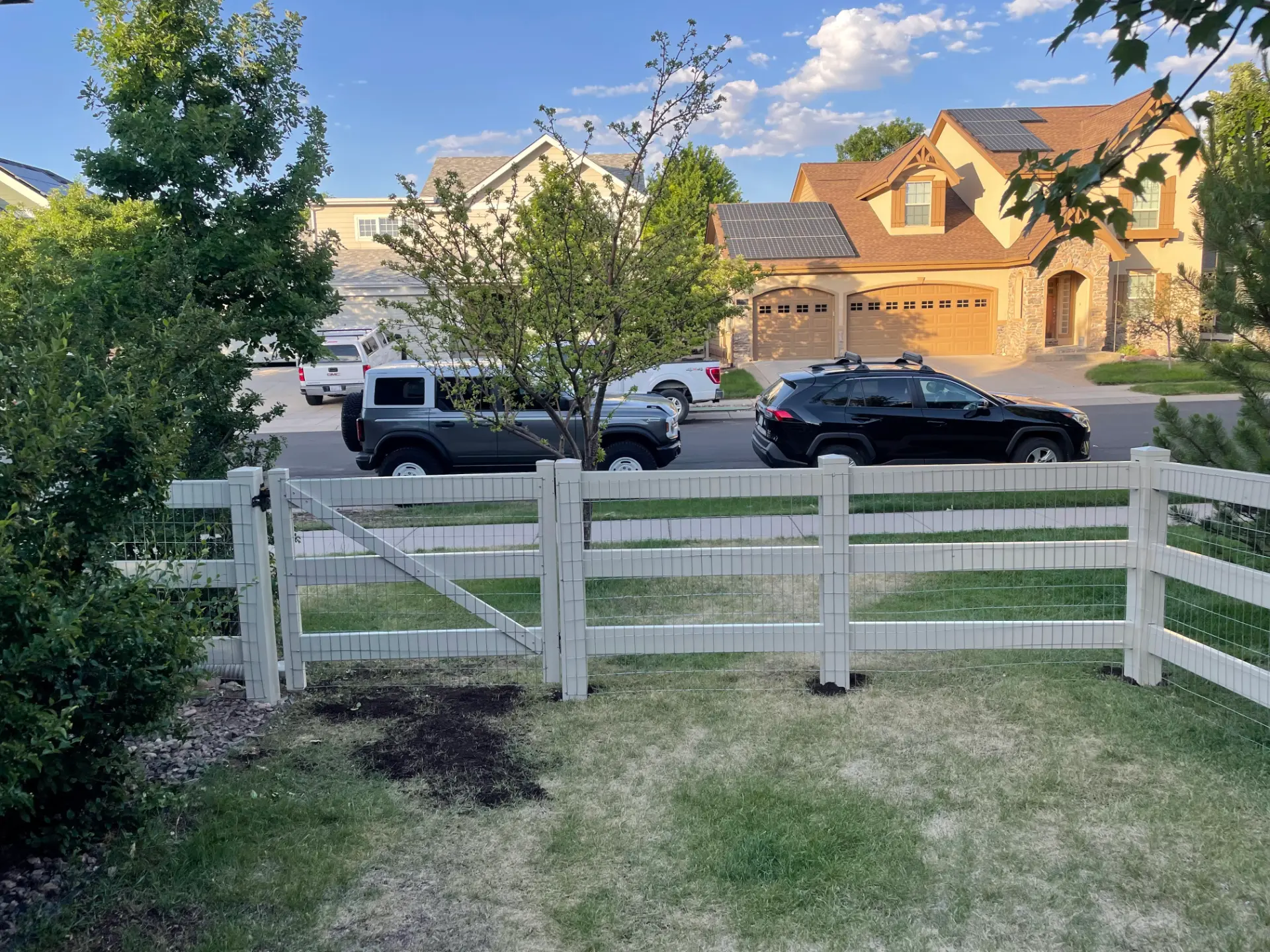 White three-rail fence with wire mesh enclosing a front yard