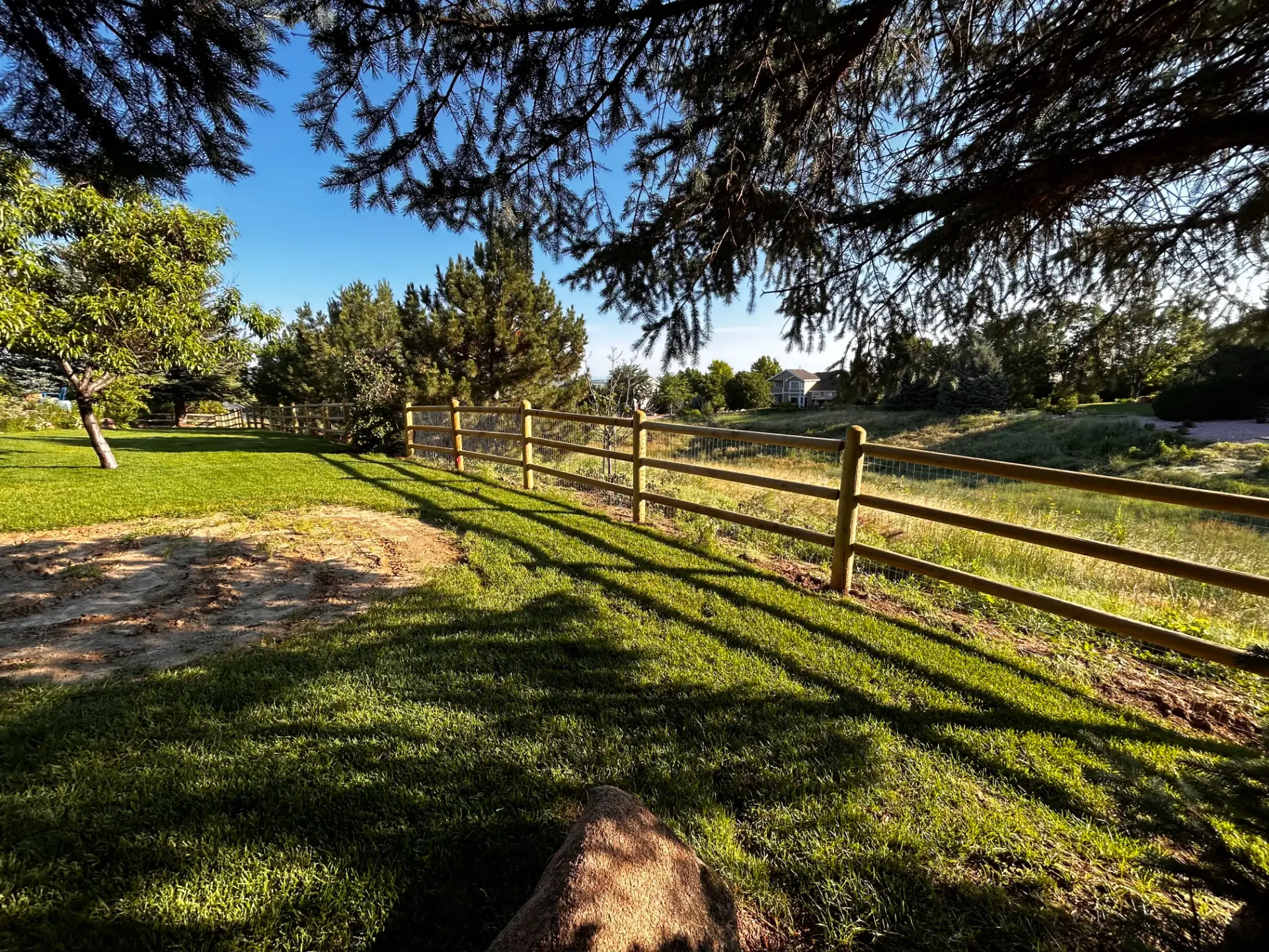 Long round-post split rail fence following a green residential property line