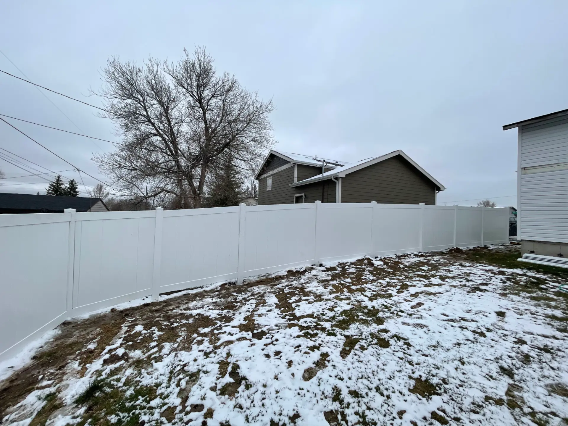 Long white vinyl privacy fence installed across a snowy backyard