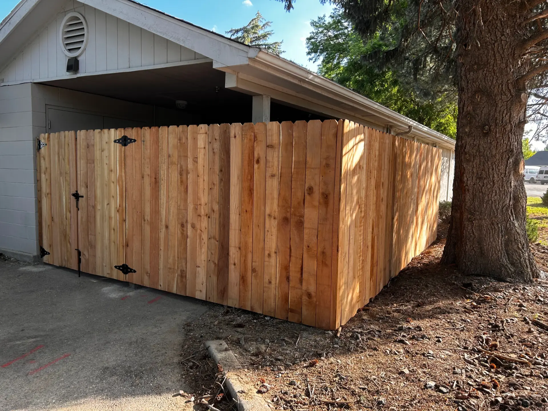 Custom cedar privacy enclosure with black gate hardware beside a garage