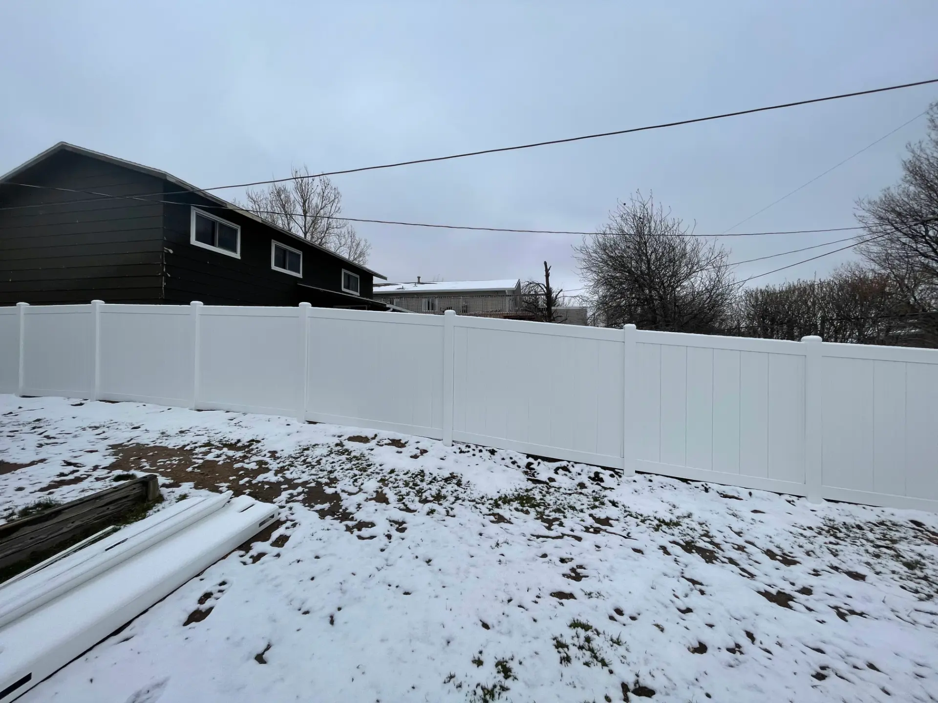 White vinyl privacy fence following a gently sloped snowy yard